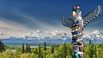 A totem pole, with a forest and mountain landscape